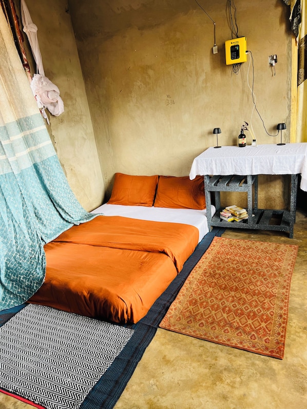A room with a bed, a small table with a white tablecloth, a patterned rug, and a wall-mounted device.