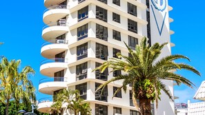 Ein mehrstöckiges Hotel mit Balkonen, einer Palme und blauem Himmel.