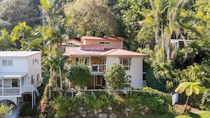 Ein zweistöckiges Haus mit Balkon, umgeben von üppiger Vegetation und Bäumen.