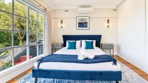 Een moderne slaapkamer met een groot bed, uitzicht op groen en een plafondventilator.