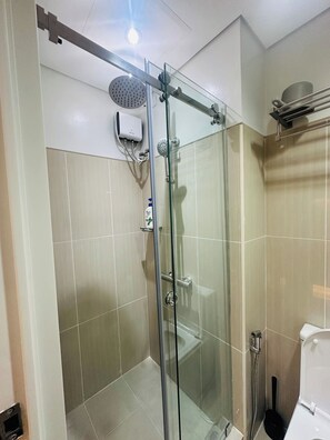 A glass-enclosed shower with a handheld showerhead, a handheld shower attachment, and a wall-mounted faucet. - Cozy Scandinavian-inspired Condo With Balcony Facing SM Mall of Asia (Pasay)