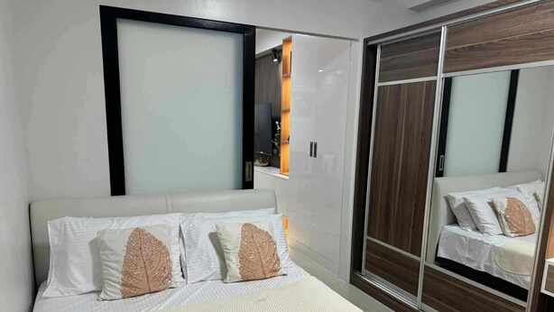 A modern bedroom with a bed, white bedding, and a large mirror reflecting the room. - Cozy Scandinavian-inspired Condo With Balcony Facing SM Mall of Asia (Pasay)
