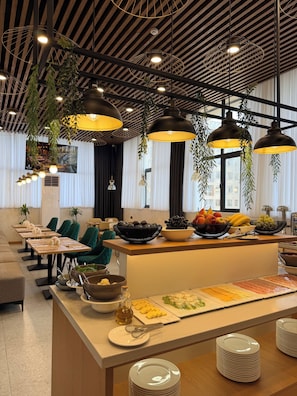 Un espace de restauration moderne avec une longue table, de nombreuses chaises, des plantes suspendues et une variété d’aliments exposés.