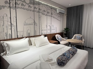 Une chambre d’hôtel avec un grand lit, une table ronde, une chaise et un mur orné d’une fresque décorative.