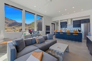 A modern living space with a large sofa, a coffee table, and a kitchen area with a bar. - Desert Contemporaine - Stargazer's Oasis - Hot Tub - Desert Views (Joshua Tree)