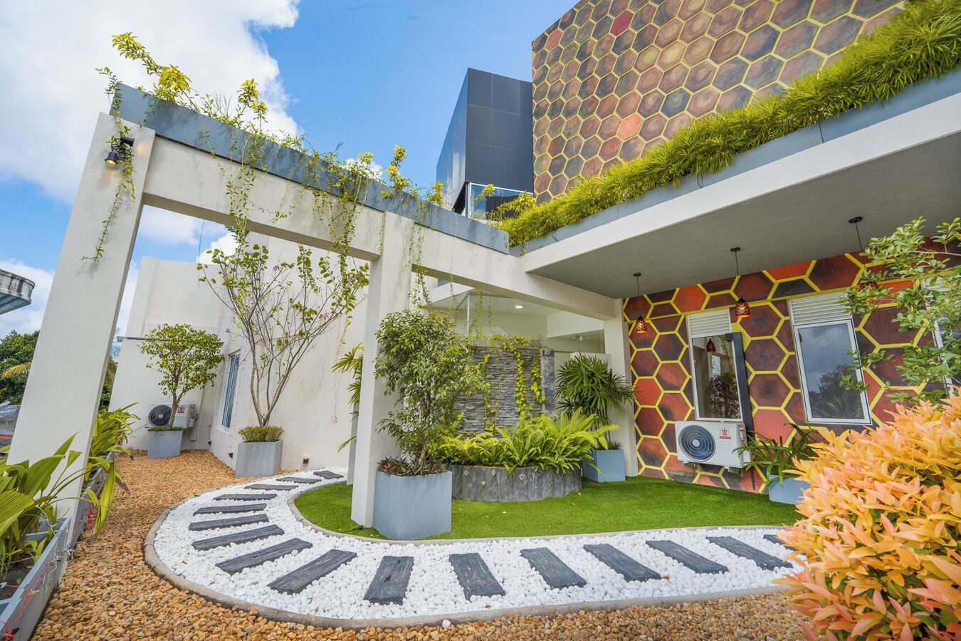 A modern building with a unique hexagonal patterned facade, a central courtyard with a circular pathway, and various potted plants.