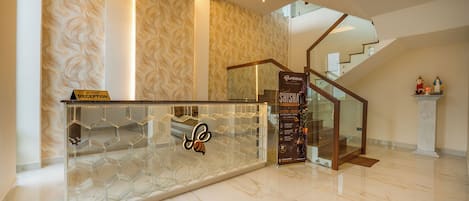 Ein Hotel-Empfangsbereich mit modernem Design, inklusive einer Rezeption mit Glastisch und einem Logo, einer Treppe und einem Empfangsschild.