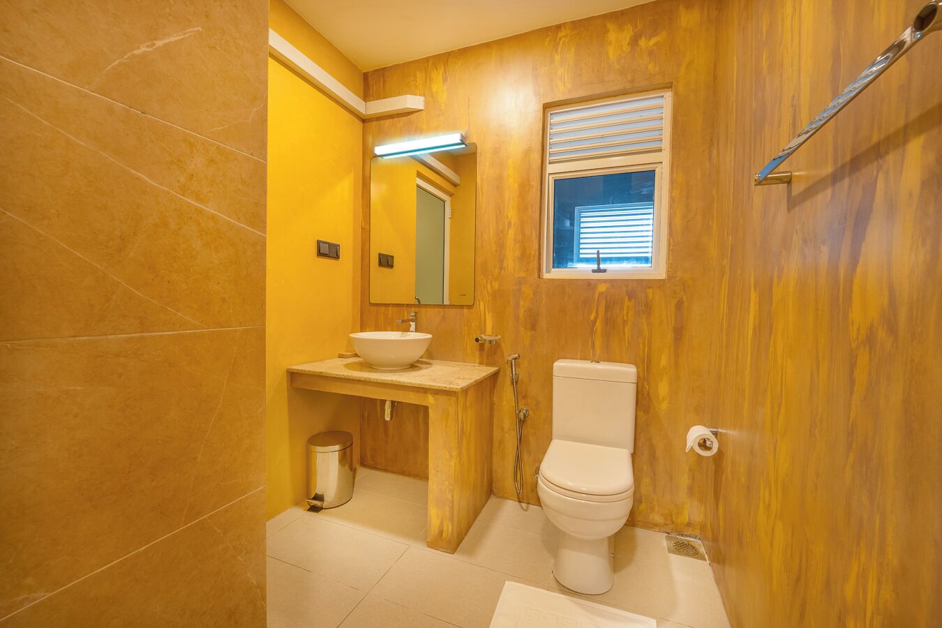 Un baño con tocador de madera, un lavabo blanco, un inodoro y una ventana con persianas.