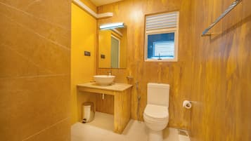 Un baño con tocador de madera, un lavabo blanco, un inodoro y una ventana con persianas.