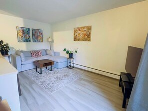 A modern living room with a sofa, coffee table, and a small side table with a plant. - 1 Bedroom Condo - Perfect Calgary Base (Calgary)