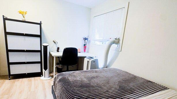 Een slaapkamer met een bed, een bureau, een stoel, een radiator en een kast.
