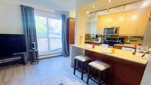 Een moderne keuken met een centraal eiland, barkrukken, een flatscreen televisie en een schuifpui naar een balkon.