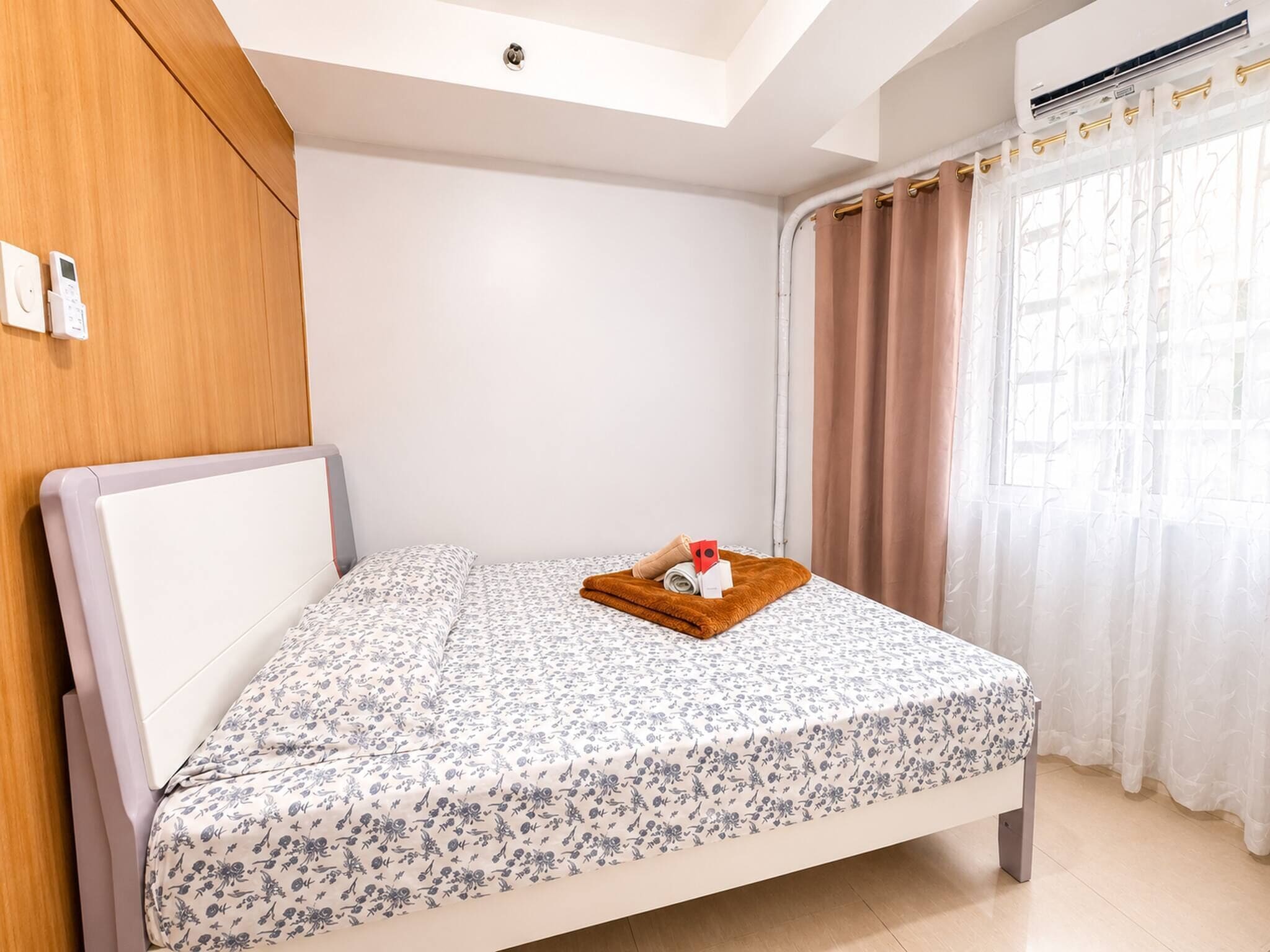 A single bed with a floral bedspread, a brown throw blanket, and a small red object on it.