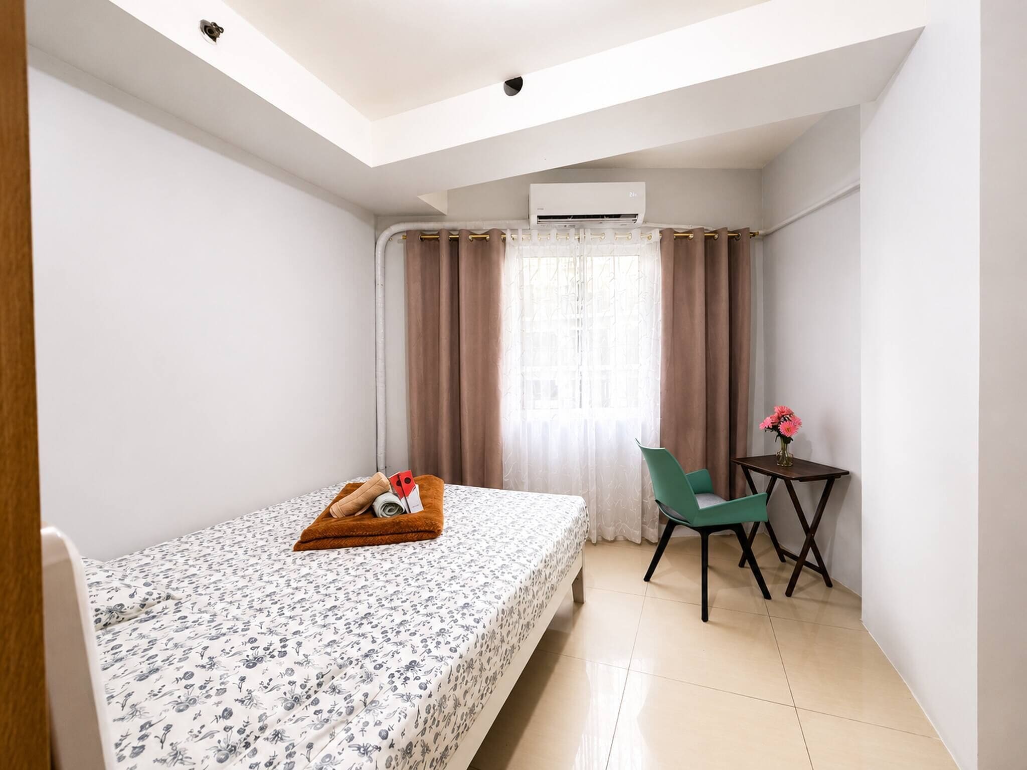 Een hotelkamer met een bed, een stoel, een tafeltje en een raam met gordijnen.