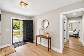 Ein Flur mit Holzboden, einer schwarzen Tür, einem kleinen Tisch mit Lampe und einem Spiegel an der Wand.