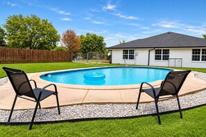 Ein Garten mit Schwimmbecken, zwei Liegestühlen, einem Holzzaun und einem Haus mit dunklem Dach.