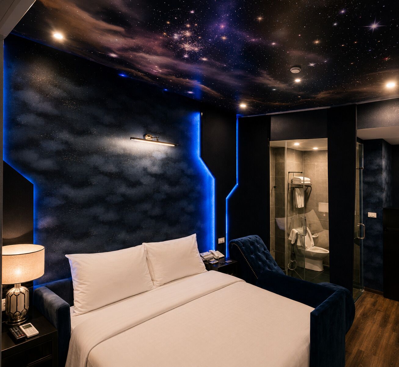 A bedroom with a bed, bedside table, and a nightstand. There is a bathroom with a shower and a toilet visible through a glass partition.