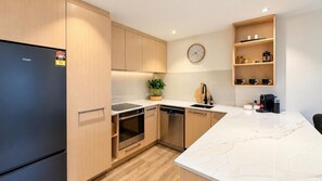 A modern kitchen with a built-in refrigerator, oven, and dishwasher, wooden cabinets, a marble countertop, and a clock on the wall. - Lakeview on Goldrush (Queenstown)