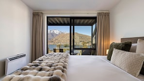 A hotel room with a large bed, a view of mountains, and a balcony with a table and chairs. - Lakeview on Goldrush (Queenstown)