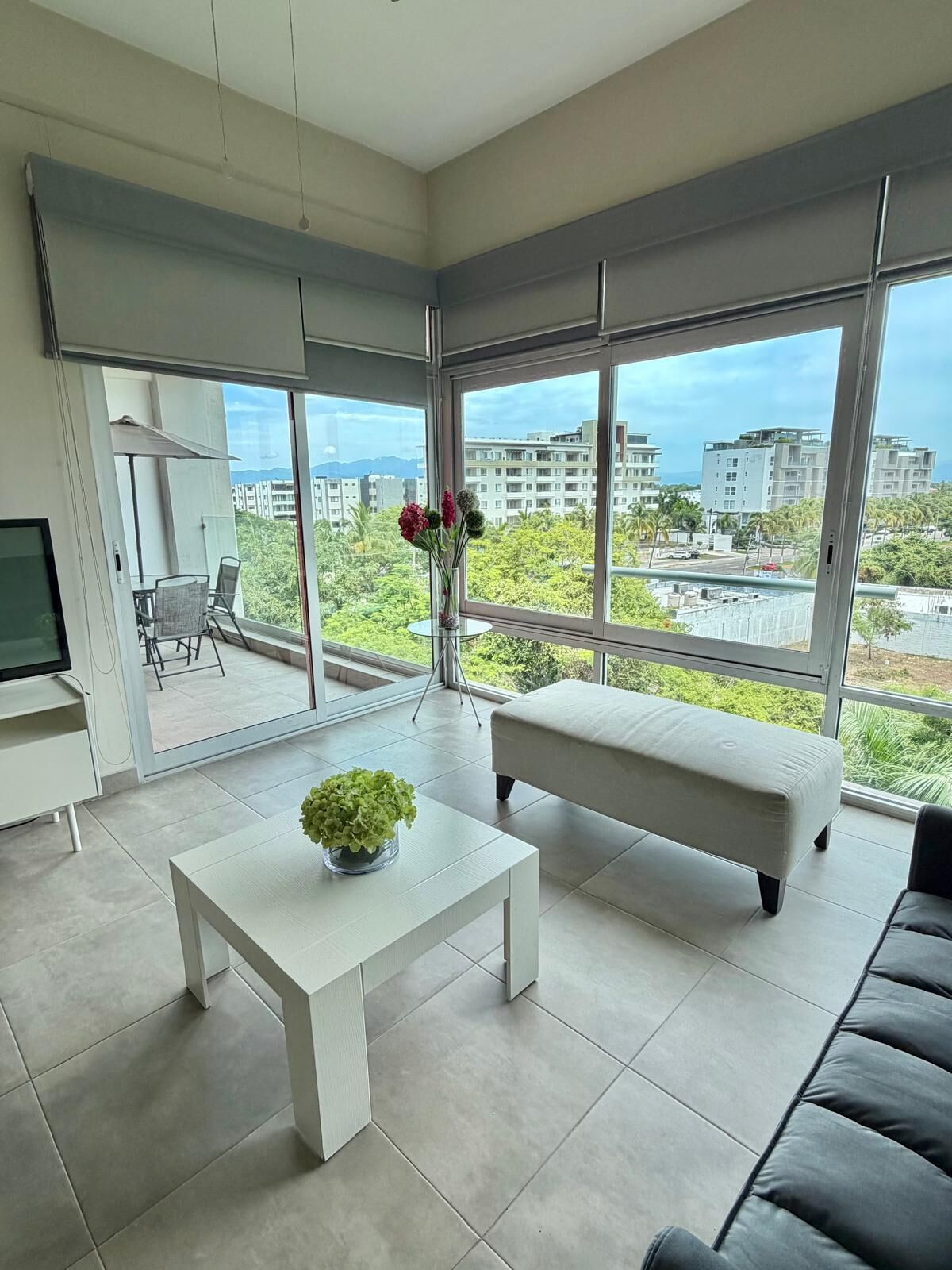Ein modernes Wohnzimmer mit großem Fenster, einer Couch, einem Couchtisch und einem Fernseher.
