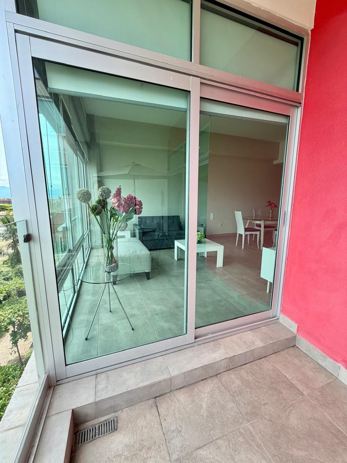 A modern interior with a glass door leading to a balcony, a dining area with a table and chairs, and a sofa.