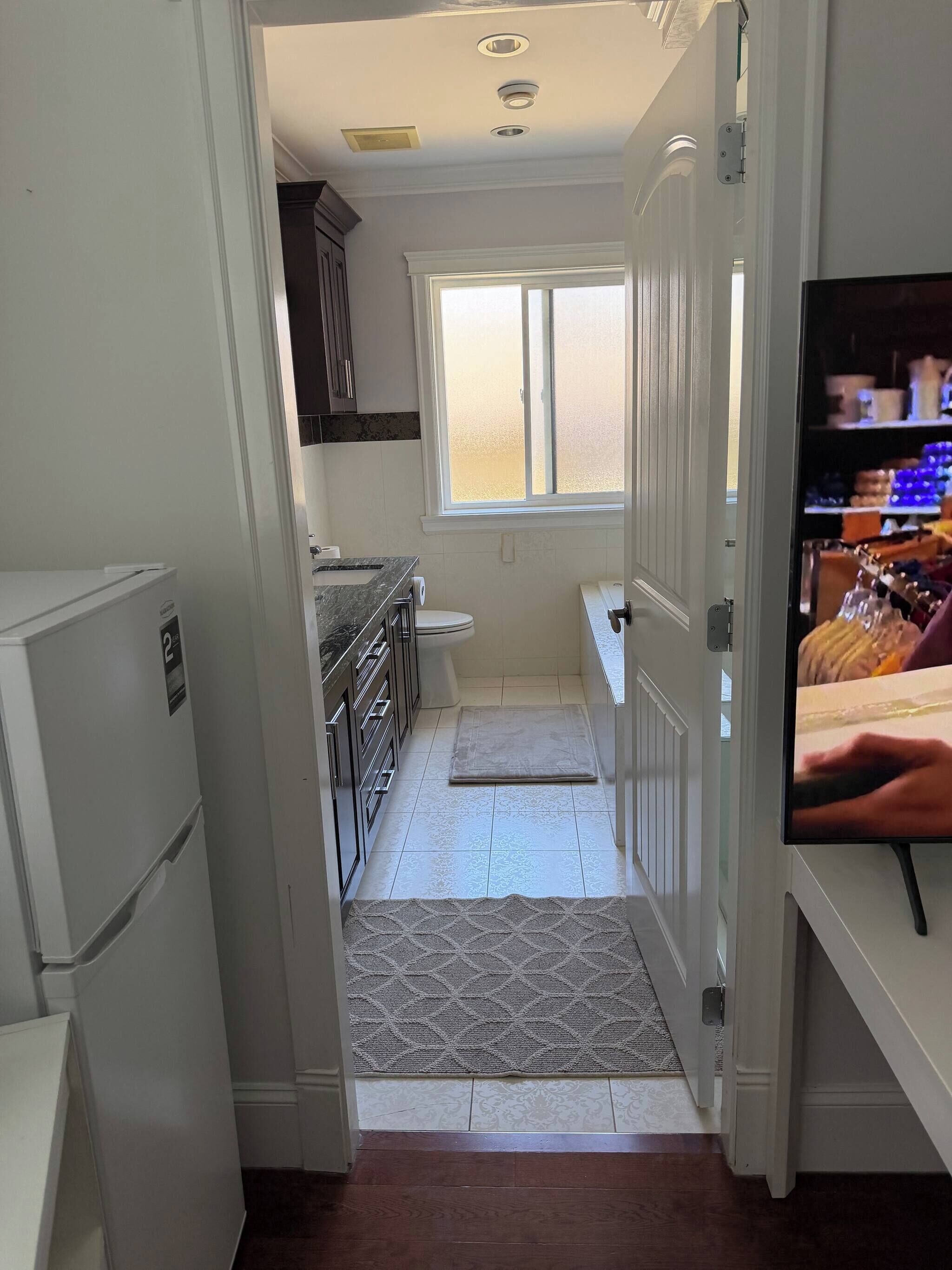A narrow kitchen with a refrigerator, a sink, and a window.