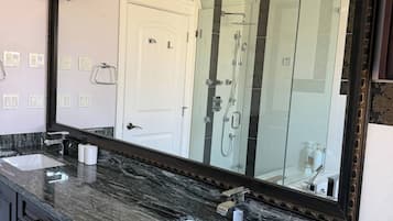 A bathroom with a large mirror, two sinks, a shower, and a marble countertop.
