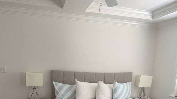 A bedroom with a bed, two bedside tables, a ceiling fan, and a window.