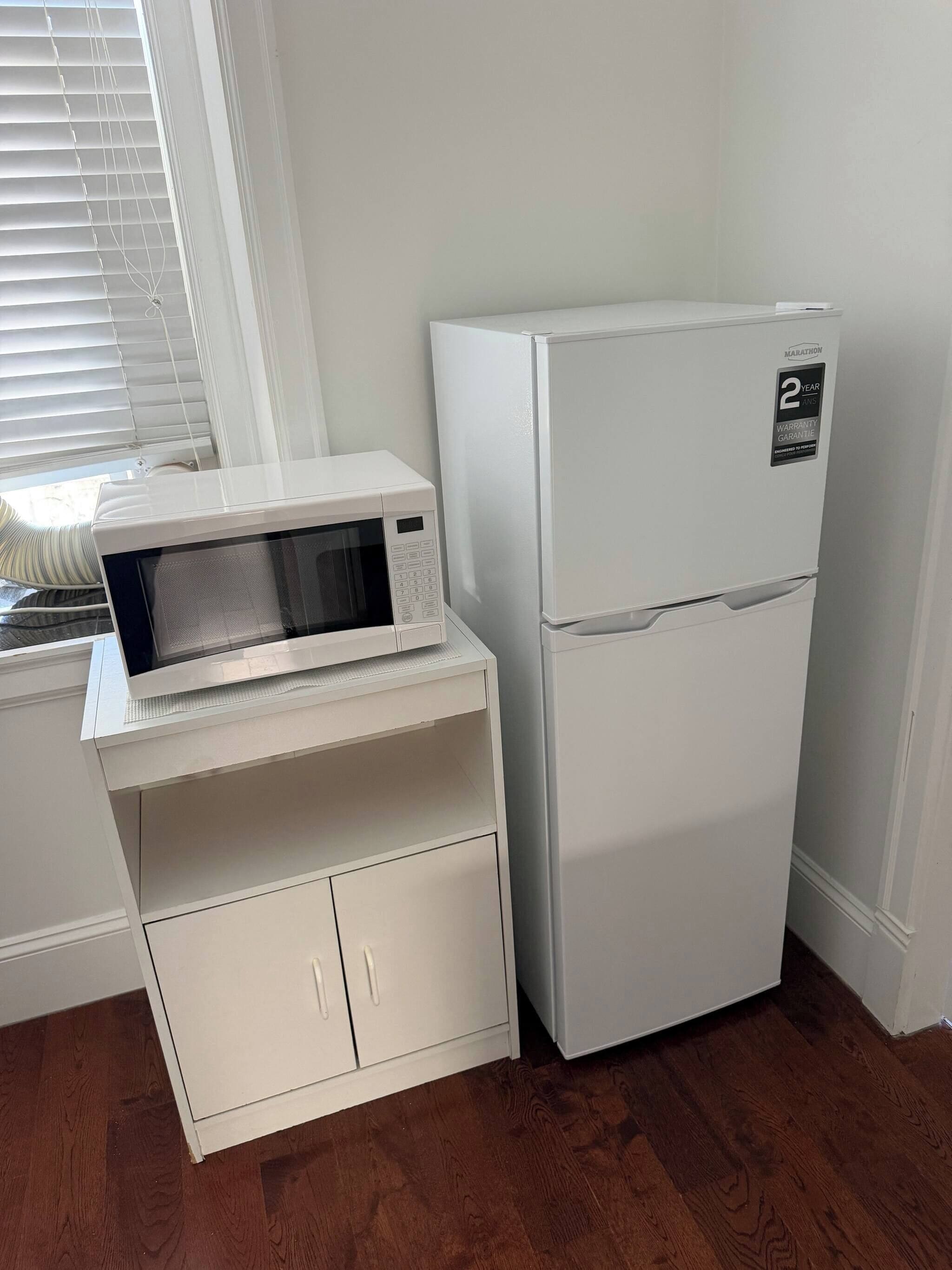 A compact kitchenette with a microwave, refrigerator, and a small cabinet.