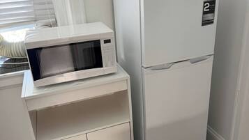 A compact kitchenette with a microwave, refrigerator, and a small cabinet.