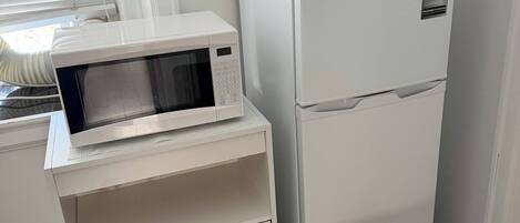 A compact kitchenette with a microwave, refrigerator, and a small cabinet.