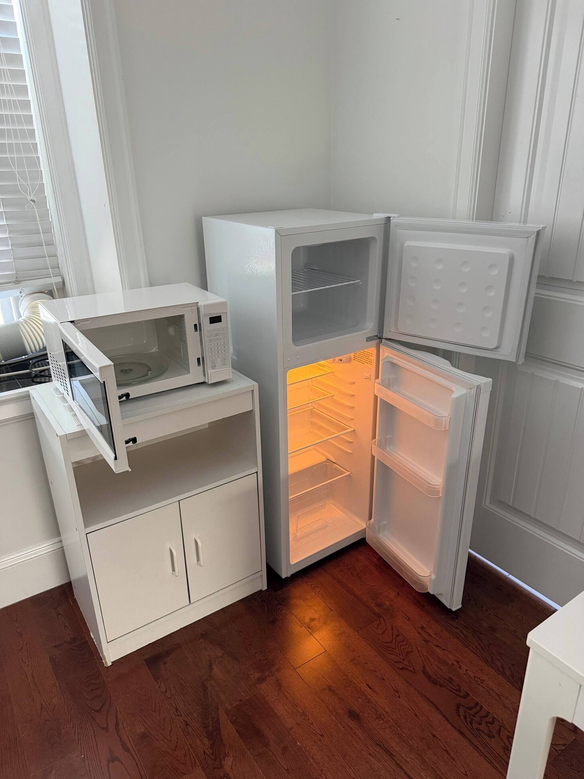 A corner of a room with a white refrigerator, a microwave, and a wooden floor.