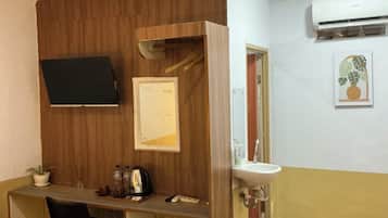 Habitación de hotel con cama, escritorio, silla, televisor, espejo, lavamanos y aire acondicionado.