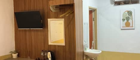 A hotel room with a bed, a desk, a chair, a TV, a mirror, a sink, and an air conditioner.