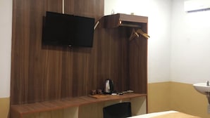 A hotel room with a bed, a wooden desk, a television mounted on the wall, and a bathroom with a sink.