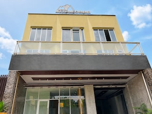 A hotel with a yellow facade, a balcony with glass railings, and a sign above the entrance.