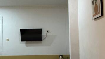 Une chambre d’hôtel avec un lit, un téléviseur à écran plat fixé au mur, une petite table avec une bouilloire et un tableau encadré au mur.