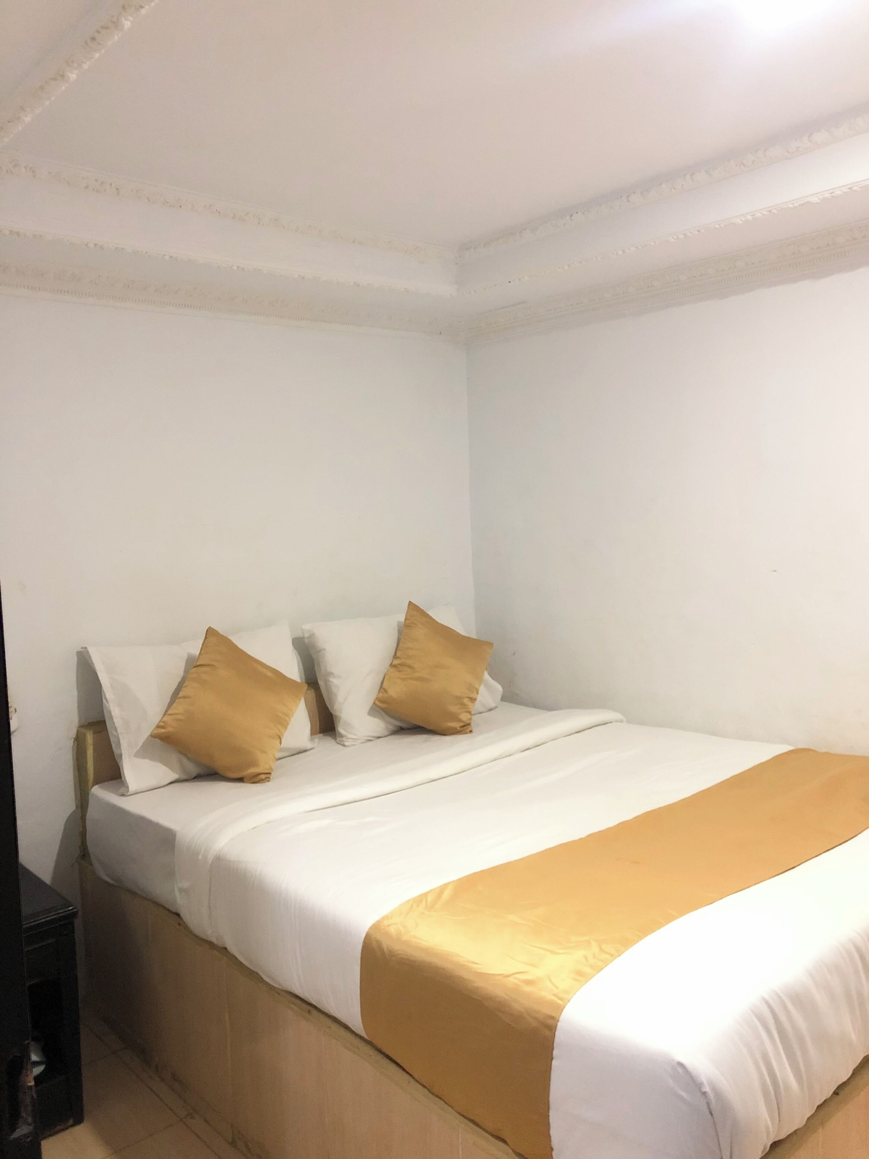 Una cama individual con una colcha blanca y dorada, dos almohadas blancas y una dorada.