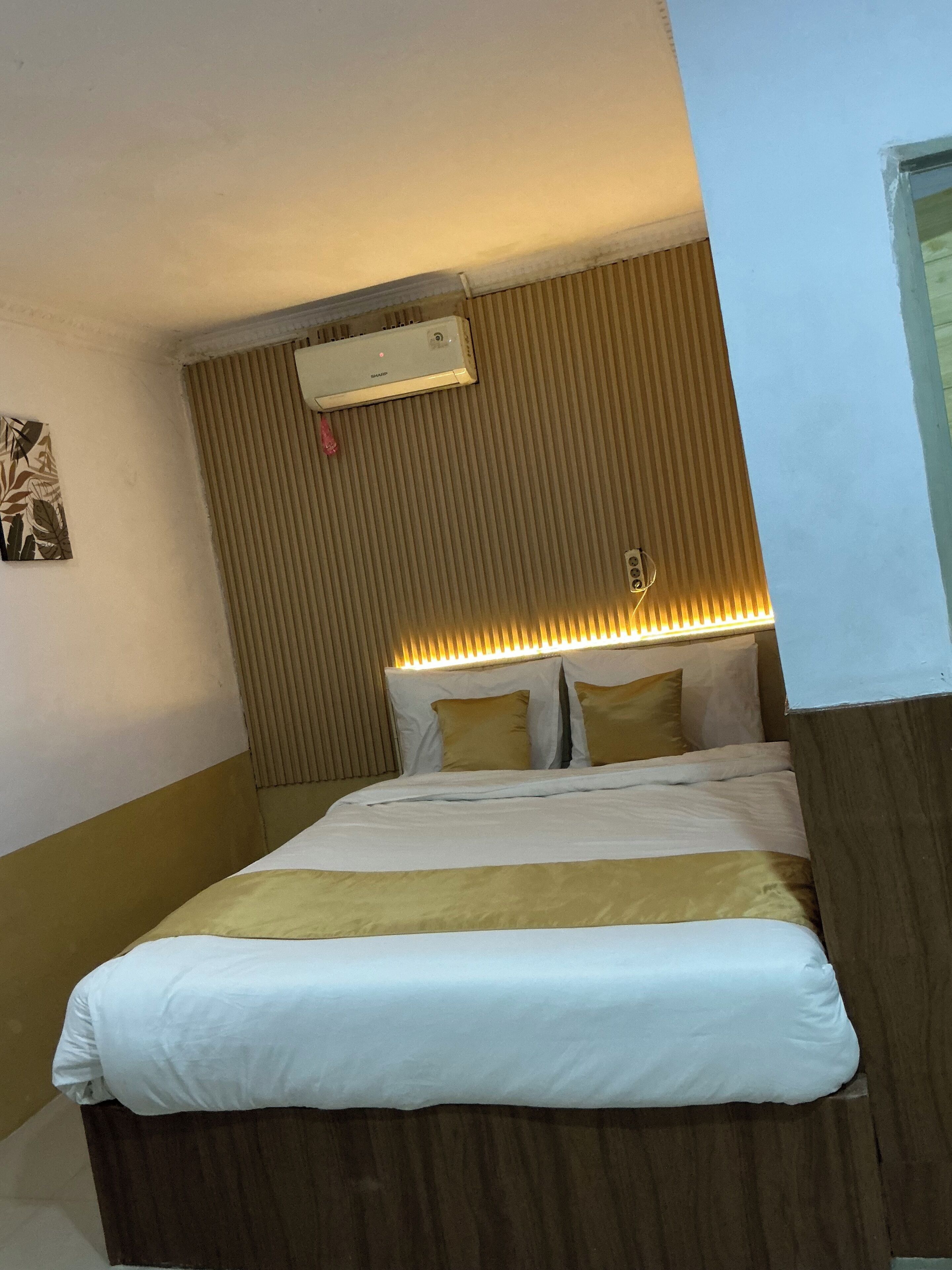 Habitación de hotel con cama, aire acondicionado de pared y cabecera con iluminación integrada.