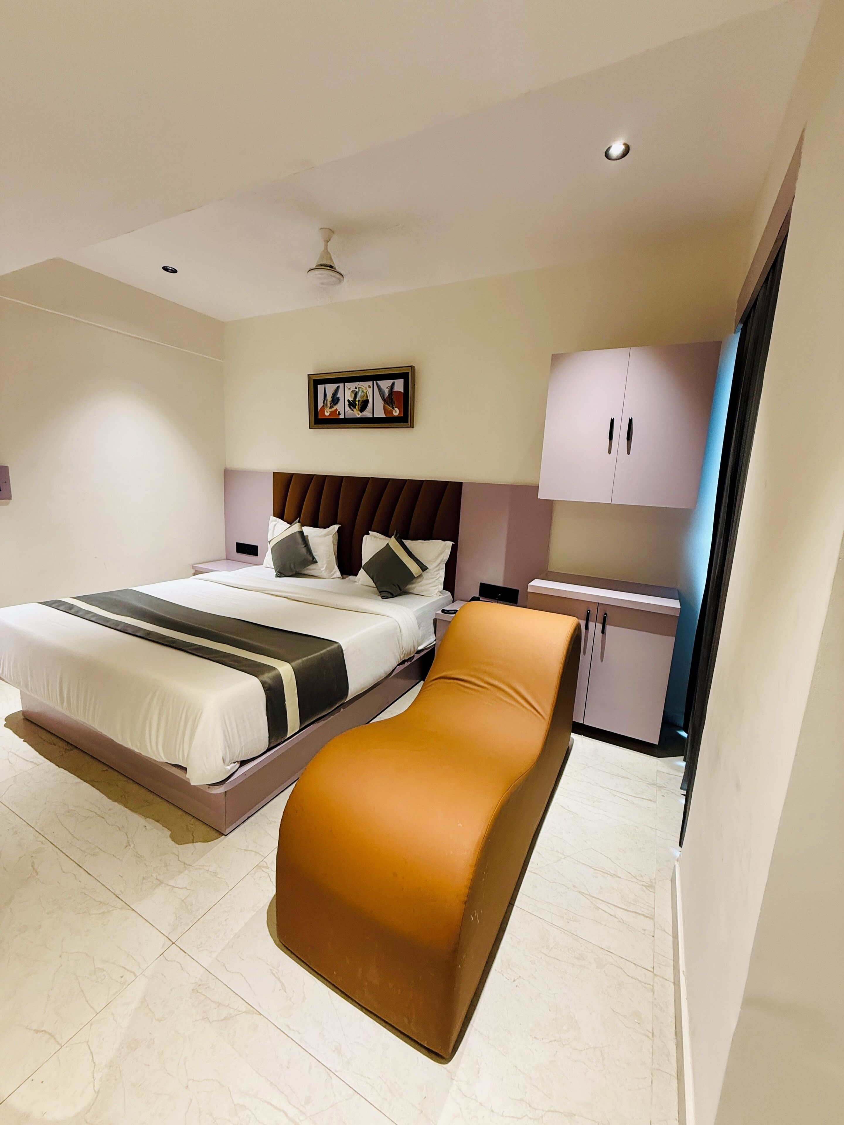 A modern hotel room with a bed, a seating area, a nightstand, and a cabinet.