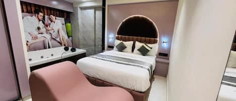 Un dormitorio moderno con cabecera curva, una cama con almohadas, una mesita de noche y un televisor montado en la pared.