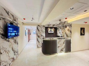 A reception area with a marble wall, a reception desk, and a flat-screen TV.