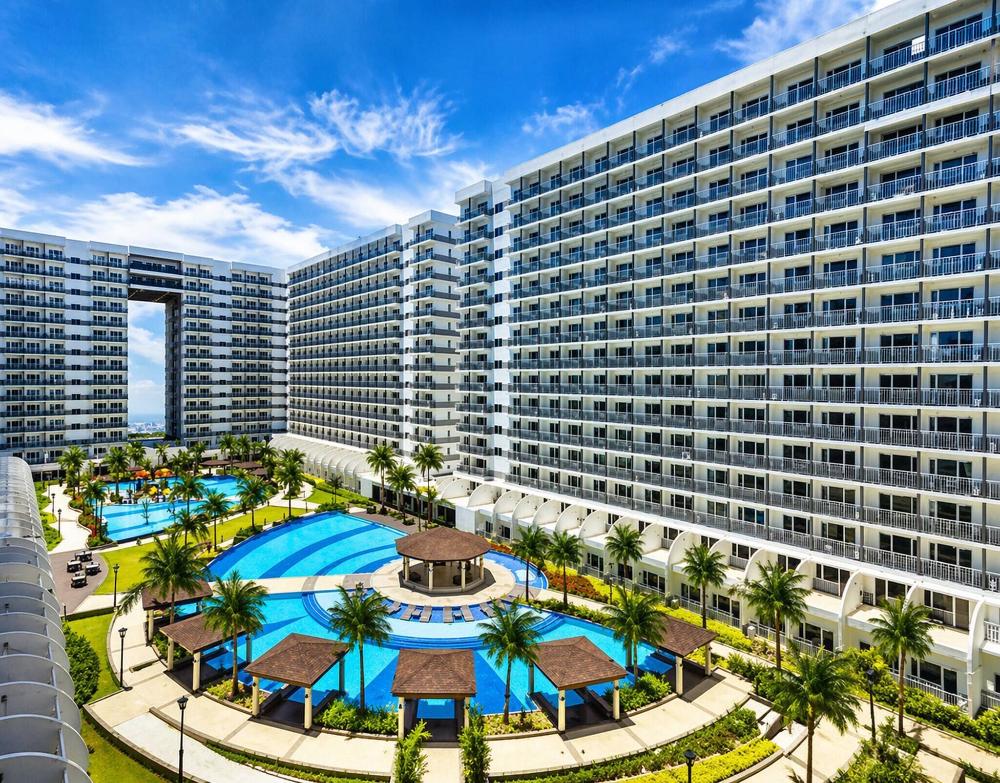Un hôtel à plusieurs étages doté d’un espace piscine central, entouré de palmiers et comprenant une piscine circulaire.