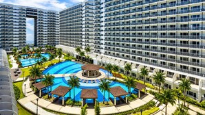 Ein mehrstöckiges Hotel mit einem zentral gelegenen Poolbereich, umgeben von Palmen und einem kreisförmigen Pool.