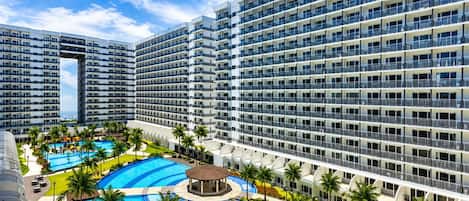 A multi-story hotel with a central pool area surrounded by palm trees and a circular pool.
