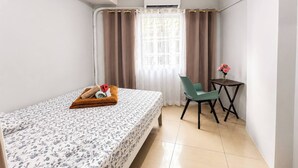 Ein kleines Hotelzimmer mit Bett, einem Tisch mit Blumenvase, einem Sessel und einer Klimaanlage.
