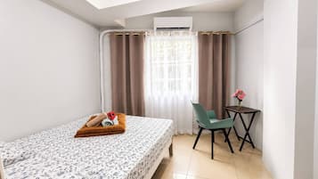 Une chambre d’hôtel de taille modeste, comprenant un lit, une petite table avec un vase de fleurs, une chaise et un appareil de climatisation.