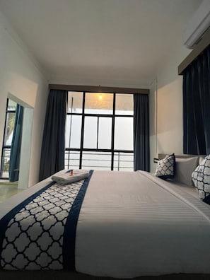 Una habitación de hotel con una cama grande, una ventana con cortinas, una mesita de noche y vistas al exterior.