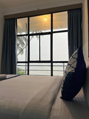 Una habitación de hotel con un ventanal grande, una cama con almohada y vista a palmeras.