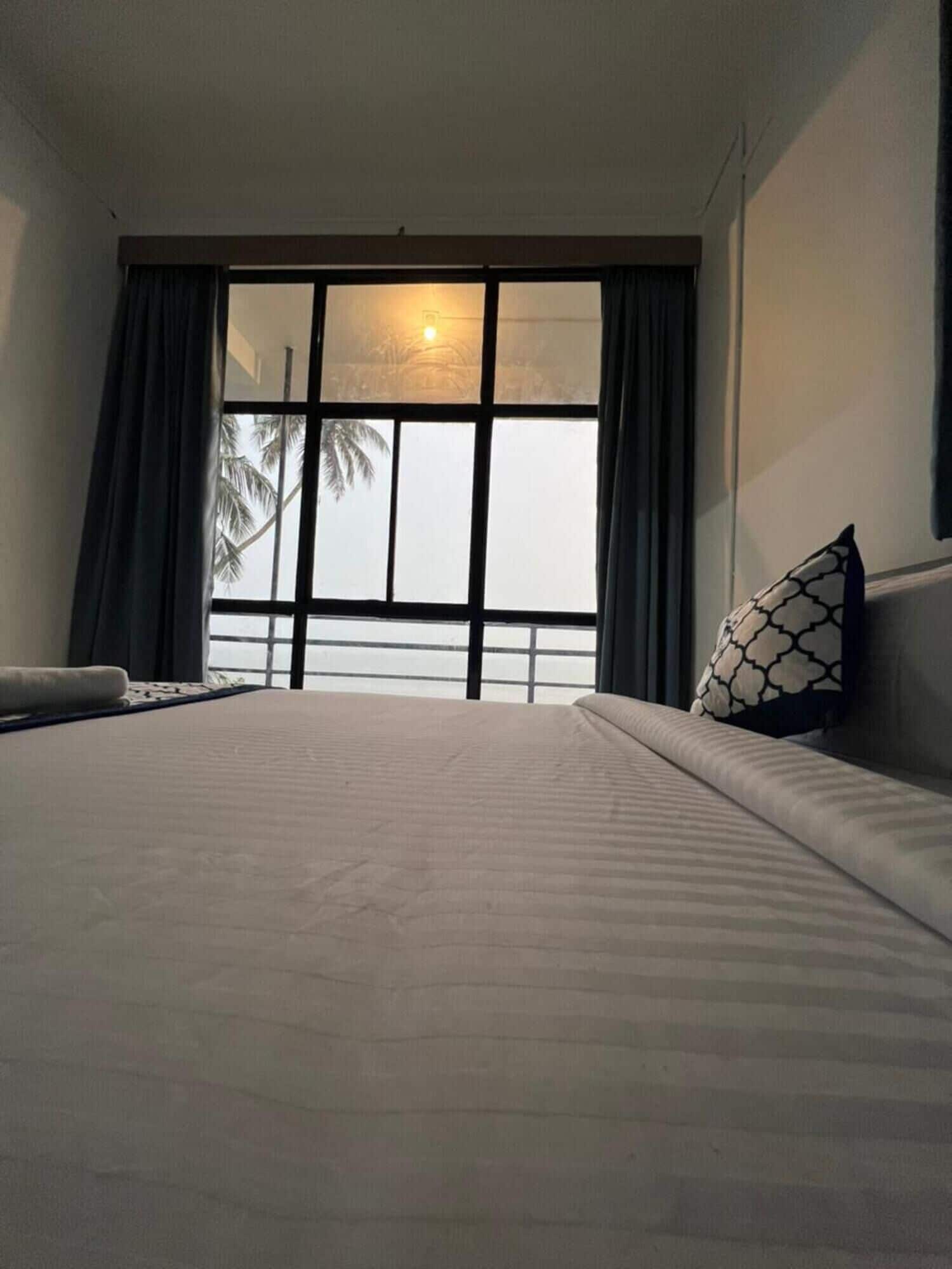 A hotel room with a large bed, a window with curtains, and a view of palm trees.